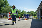 Ein Helfer des Technischen Hilfswerks mit gelber Warnweste trägt einen Pylon, um eine Einsatzstelle abzusichern. Im Hintergrund leiten weitere Pylone die Verkehrsteilnehmer an einem Fahrzeug des THW vorbei.